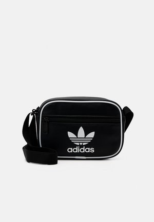 Bolso cruzado negro de Adidas con logo blanco, en forma rectangular, textura suave y ribete blanco en contraste; cuenta con un bolsillo frontal con cremallera.