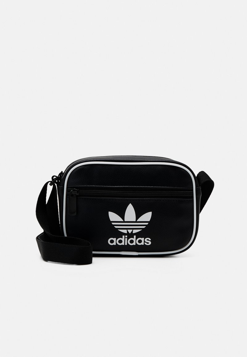 Svart Adidas axelväska med vit logotyp, rektangulär form, slät textur och kontrasterande vit kant; har en dragkedjeförsedd framficka.