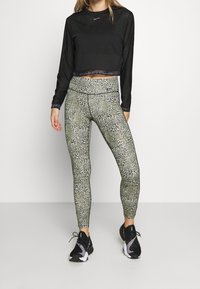 Top nero a manica lunga corto con texture a coste; leggings verdi con motivo misto di stampa animalier e motivo a griglia; scarpe da ginnastica nere.