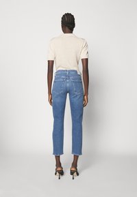 Modré džíny s vysokým pasem a rovný střih, pět kapsiček a jemné vyblednutí, v kombinaci s béžovým tričkem s krátkým rukávem.