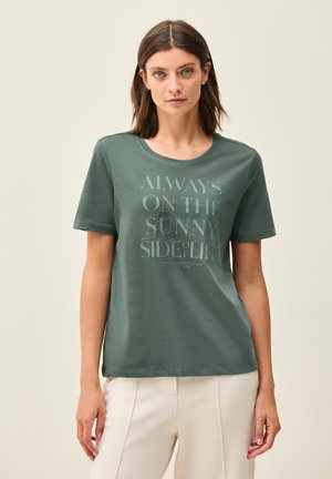 T-shirt en coton vert à manches courtes et col rond. Présente un imprimé graphique en gris clair, le texte indique "TOUJOURS DU BON CÔTÉ DE LA VIE."