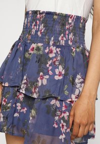 Blommig lager-skirt i blått tyg med rosa och vita blommor, med en smockad midja och lager av fladdrande volanger, lätt och flödande.