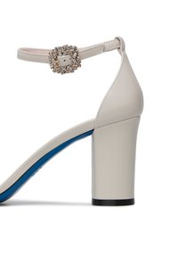 Sandal con tacco alto beige con punta quadrata, grande fibbia di strass e un accento blu. Presenta un solido tacco a blocco.