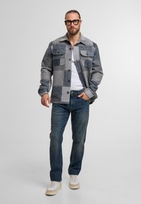 Grå og marineblå ternet skjorte med knaplukning, to brystlommer, parret med mellemblå jeans og hvide sneakers. På en ensfarvet baggrund.