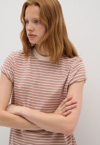 Camiseta a rayas en colores crema y óxido, con mangas cortas y escote redondo. El material parece ligero y texturizado.