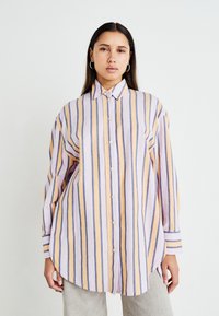 Chemise à rayures avec des rayures verticales violettes, orange et blanches, à manches longues et à ourlet incurvé. Fabriquée en tissu léger.