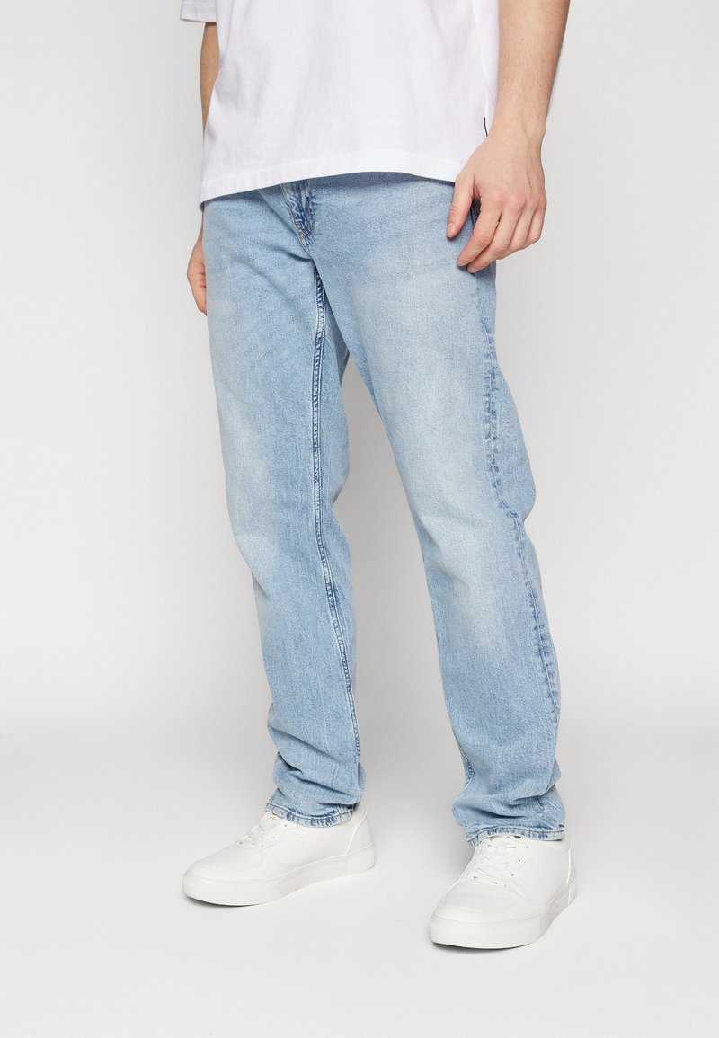 Light blue denim jeans with a straight leg cut, featuring a classic five-pocket design, worn with white sneakers and a white t-shirt.