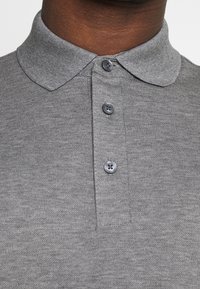 Grå polo med mjukt, texturerat tyg, krage och tre knappstängningar framtill.