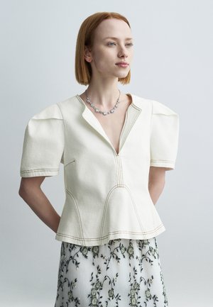 Hvit bomullstopp med korte puffermet ermer, dyp utringning og kontrasterende sømmer, kombinert med et gjennomsiktig skjørt med blomsterprint.