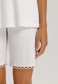 Pantalones cortos de algodón blancos con detalles de dobladillo en forma de ondas, mostrados combinados con una blusa blanca suelta, destacando la textura de la tela y el diseño sencillo.
