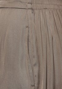 Brązowa plisowana tkanina o miękkiej fakturze, z elastycznym paskiem w talii i bocznymi kieszeniami dla dodatkowej funkcjonalności.