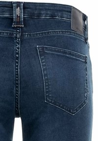 Granatowe dżinsy z klasycznym wzorem tylnej kieszeni, teksturowanym materiałem i skórzaną metką na pasku.