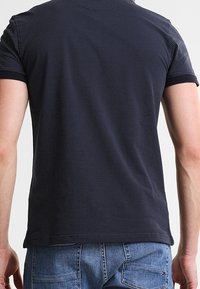 Polo à manches courtes marine avec un motif de points texturé, featuring un col et des poignets côtelés. Le matériau semble respirant et décontracté.