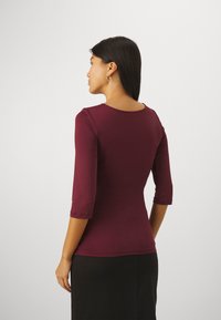 Burgundy fitted long-sleeve top with a round neckline, featuring ruched details on the sleeves and a smooth texture.