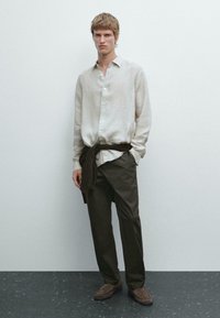 Linnen shirt in lichtbeige met een knoopsluiting aan de voorkant en lange mouwen, gecombineerd met donkerbruine broeken en bijpassende suède schoenen.