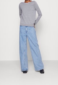 Harmaa pitkähihaisen neuleen, jossa on pyöreä kaula-aukko, on yhdistetty vaaleansiniisiin leveisiin farkkusalkaisiin ja mustiin paksupohjaisiin kenkiin.