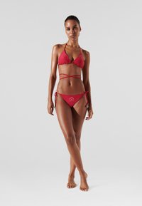 Rode bikini met driehoekige top en verstelbare bandjes, met een gladde textuur en grafische print op de onderkant; minimalistisch ontwerp.