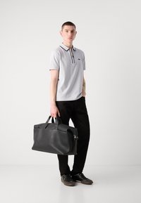 Maglietta polo grigia con rifiniture nere, pantaloni neri e una borsa in pelle nera texturizzata. Le scarpe sono scure con un motivo sobrio.