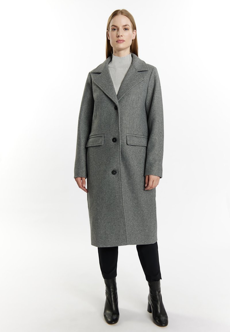 Grau Wollmantel mit Reverskragen, einreihigem Design, zwei Taschen vorne und schwarzen Knöpfen. Getragen über einem hellgrauen Oberteil und schwarzen Hosen.