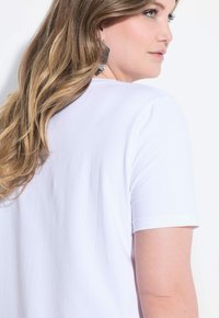 Hvid bomulds t-shirt med korte ærmer, der har en rund halsudskæring. Udsigten viser en delvis profil, der fremhæver det glatte stof og den afslappede pasform.