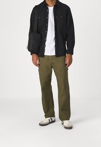 Black button-up shirt over a white t-shirt, olive green pants, and white sneakers with black accents. A small black shoulder bag is worn.