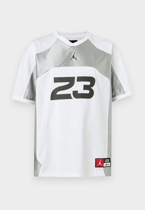 Biała i szara sportowa koszulka z krótkim rękawem z czarnym numerem 23 oraz małymi czerwono-czarnymi naszywkami z logo Jumpman.