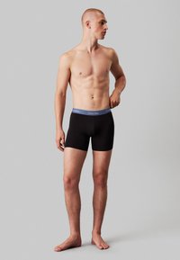 Fekete boxer alsónemű szürke Calvin Klein derékrésszel. Az anyag simának és rugalmasnak tűnik, szoros illeszkedésre tervezve.