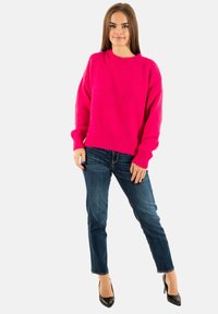 Maglione oversized fucsia a maglia con collo rotondo, finitura testurizzata, abbinato a jeans in denim blu e tacchi neri a punta.