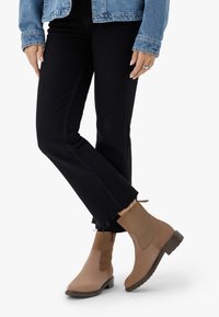 Rudos kulniukus turinčios ankle botai su susipynusiais elastiniais intarpais, tekstūruotu paviršiumi ir žemu bloku kulnu, derinami su juodomis ištrintomis džinsomis ir džinsiniu švarku.