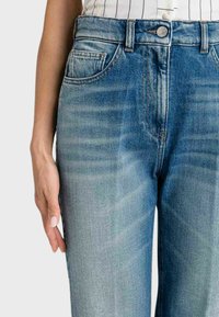 Jeans in denim blu con una finitura leggermente sbiadita, dotati di cinque tasche, chiusura a bottone e cuciture a contrasto lungo le cuciture.