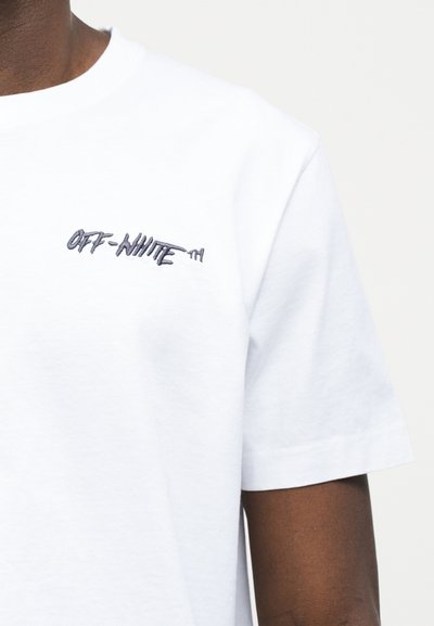 Άτομο που φοράει λευκό t-shirt με κοντά μανίκια και μικρό μαύρο κεντημένο λογότυπο "OFF-WHITE" στο πάνω μέρος του στήθους.