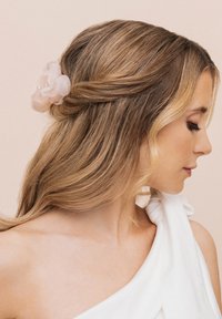 Accessorio per capelli floreale di colore rosa chiaro, realizzato in morbido tessuto, con petali traslucidi e dettagli in perle, indossato su capelli lunghi e mossi su uno sfondo neutro.