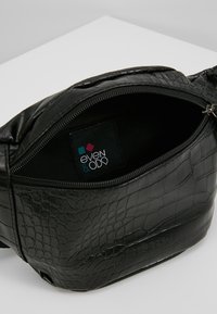 Černá kabelka z umělé kůže s krokodýlím vzorem, zipovým uzávěrem a látkovou štítkem uvnitř. Kompaktní design, vhodný pro každodenní použití.