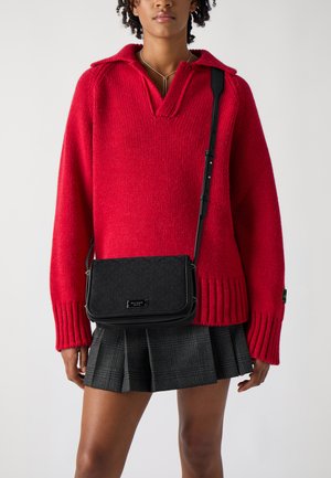 Black crossbody bag with a textured pattern, silver hardware, and a rectangular shape. Worn over a red sweater with ribbed cuffs.