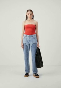 Top sem alças vermelho, jeans de brim azul claro com bolsos, mala texturizada preta e sapatilhas pretas com riscas brancas e solas de madeira.