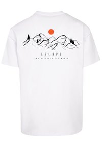 White cotton t-shirt featuring a mountain graphic, black outlines, an orange sun, and the text "ESCAPE AND DISCOVER THE WORLD" below.