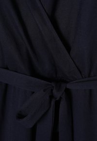 Gros plan d’un vêtement portefeuille bleu marine foncé noué à la taille avec une ceinture en tissu en un noeud simple.