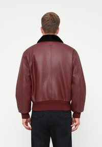 Burgundi bőrkabát fekete műszőrme gallérral, bordázott mandzsettával és derékkal, sima textúrával és egyenes hátrész kialakítással.