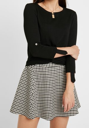 Zwarte lange mouwen top met knoopdetails op de manchetten, gecombineerd met een zwart-witte ruitjes skaterrok, die een gladde textuur en een getailleerd ontwerp heeft.