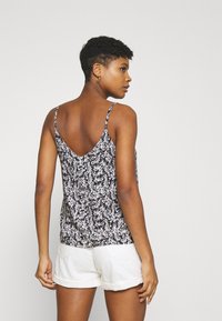 Camisola preta floral com alças finas, apresentando um design de costas em V. O tecido exibe um pequeno padrão de flores brancas por toda a peça.