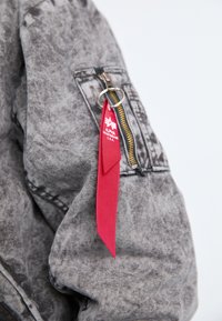 Gray denim jacket with a zipper, featuring a red tag attached by a keyring. The fabric has a textured, worn appearance.