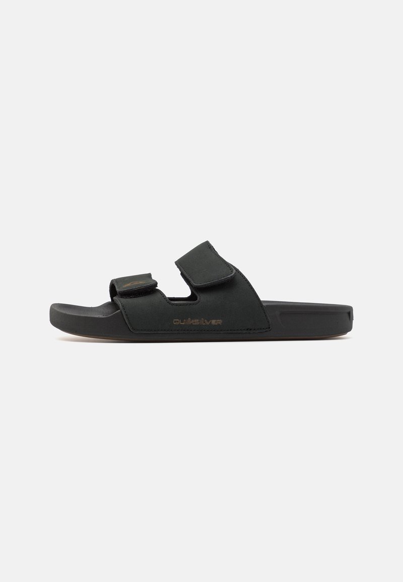 Sandale noire avec deux brides réglables en Velcro, semelle en caoutchouc et détail de logo en relief. Fabriquée en matériau semblable à du daim avec un design plat.