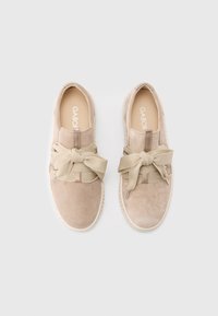 Scarpe beige in camoscio senza lacci con un grande fiocco elastico beige annodato sulla parte superiore. Suola in gomma e cuciture tono su tono.