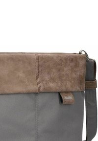 Bolso de hombro de lona gris con una solapa de cuero sintético marrón, con detalles de costura y una correa ajustable. Etiqueta de la marca visible.