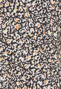 Motif floral abstrait en noir et blanc avec de petites touches orange et jaune sur une surface textile texturée.