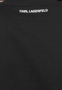 Svart bomullst-shirt med ribbad struktur och rund halsringning, med "KARL LAGERFELD"-logotyp tryckt i vitt på baksidan.