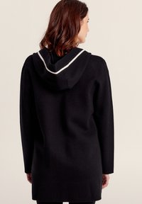 Felpa nera con un fit lungo, caratterizzata da un dettaglio a doppia striscia bianca sul cappuccio. Realizzata in un tessuto morbido con un design minimalista.