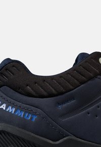 Marineblå semsket fjellsko med svart tekstilkrage, med blå logo detaljer og teksturert polstring rundt ankelen for komfort og støtte.