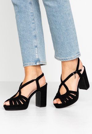 Zwarte suède sandalen met hoge hak en een bandjesontwerp, voorzien van een blokhak en een enkelbandje met een zilveren bedelaccent.