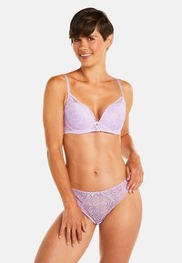 Soutien-gorge en dentelle lavande et thong assorti, avec des motifs floraux, des bords festonnés et un détail de nœud décoratif au centre du soutien-gorge.